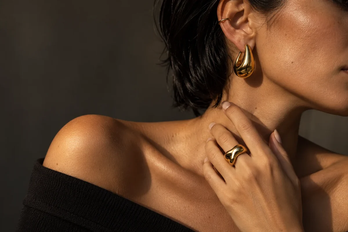 Sculptural gold earrings and a ring worn in warm natural light